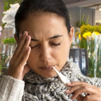 Dame met thermometer in de mond en bloemen in de achtergrond