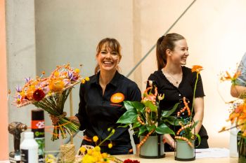 Twee dames achter een tafel aan het werk met een bloemstuk